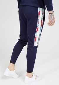 Marine joggers met een bloemrijk zijpaneel, voorzien van een witte streep. De stof is glad, met taps toelopende pijpen en ribgebreide boorden. Gecombineerd met witte sneakers.