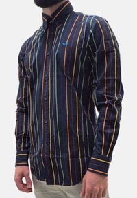 Camicia a maniche lunghe con bottoni in cotone blu navy, caratterizzata da righe verticali arancioni, verdi e gialle. Presenta un piccolo logo blu sul petto.