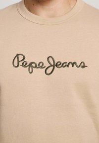 Beige sweatshirt with a crew neckline, featuring a green embroidered logo "Pepe Jeans" in a cursive style across the chest area.