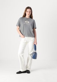 Grå t-shirt med kort ärm och kontrasterande näck, prydd med en logotyp. Matchad med vita utsvängda jeans och en liten blå handväska. Svarta skor.