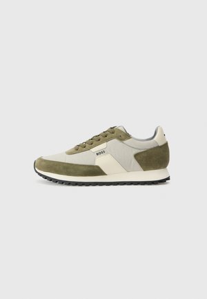 Pantofi sport verzi și bej, cu un amestec de suede și material textil, un logo alb distinct, talpă plată neagră și șireturi rotunde.