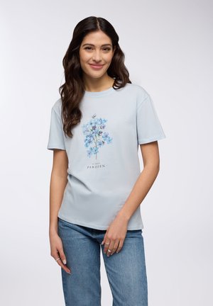 T-shirt di cotone azzurro con maniche corte, caratterizzato da un motivo floreale in tonalità di blu e viola, e la scritta "Le Jardin Parisien."
