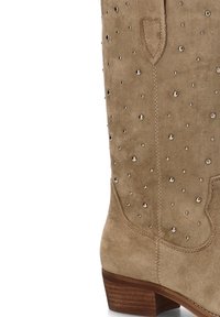 Bota de ante beige con punta redonda, caña corta y tacón bloque bajo. Decorada con tachuelas metálicas para un detalle adicional.