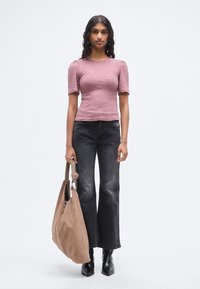 Ροζ εφαρμοστή μπλούζα με κοντά μανίκια και υφασμάτινη υφή, σε συνδυασμό με μαύρο τζιν φαρδιάς γραμμής και μεγάλη μπεζ τσάντα ώμου. Φορεμένα μαύρα μποτάκια μέχρι τον αστράγαλο.