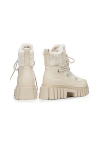Beżowe botki na grubym obcasie, wykonane z teksturowanej skóry, z miękkim futrzanym kołnierzem, z przodem sznurowanym i grubą gumową podeszwą.