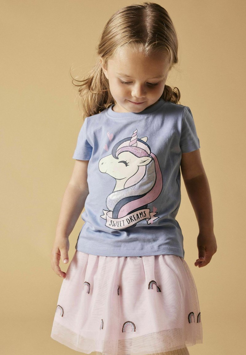 Camiseta de color azul claro con un gráfico de un unicornio y el texto "Dulces Sueños", combinada con una falda de tul rosa con patrones de arcoíris.