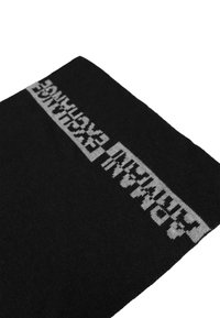 Calcetín negro de punto con un destacado diseño de texto blanco en horizontal en la parte superior. El material parece suave con una textura lisa.