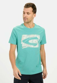 Turkis bomulds t-shirt med et tekstureret hvidt logo på en rektangulær baggrund. Kortærmet og med rund hals.