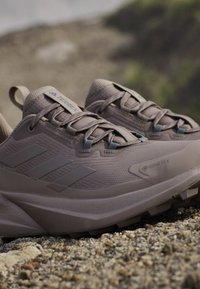 Helle braune wasserdichte Wanderschuhe mit strukturiertem Stoff, drei seitlichen Streifen, verstärkter Zehenkappe und geriffelter Gummisohle für besseren Halt.