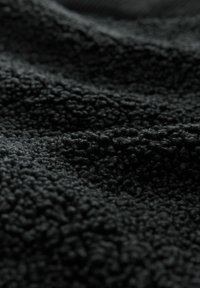 Black textured fabric with a soft, fuzzy surface and varying pile height, creating a visually rich, tactile appearance.