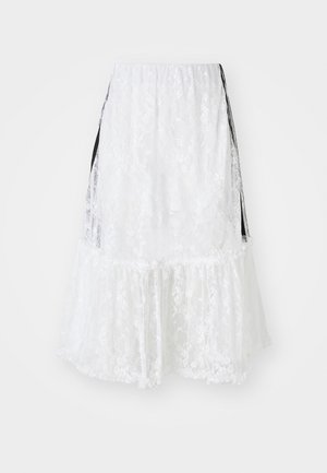 Jupe en dentelle blanche avec un design à étages, présentant un ourlet en forme de vagues et des accents latéraux noirs. Tissu texturé avec un motif floral.
