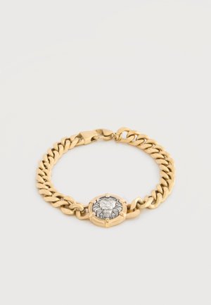 Bracelet chaîne en or avec un emblème de tête de lion en argent au centre et une fermeture à fermoir sécurisé sur fond blanc.