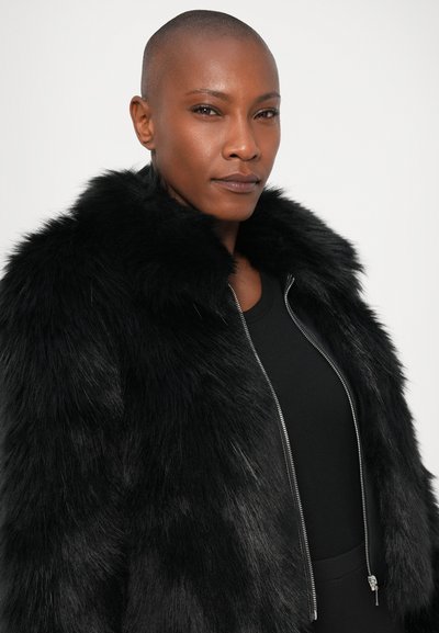 Chaqueta de pelo sintético negra con un alto cuello, cierre de cremallera frontal y una textura suave. Presenta cremalleras brillantes y un diseño ajustado.