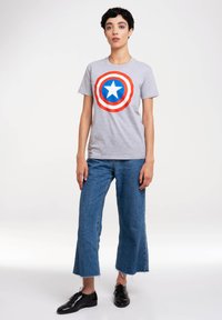 Graues T-Shirt mit rotem und blauem Captain America-Logo, das einen zentralen weißen Stern zeigt. Kombiniert mit blauen Denim-Culottes und schwarzen Schuhen.