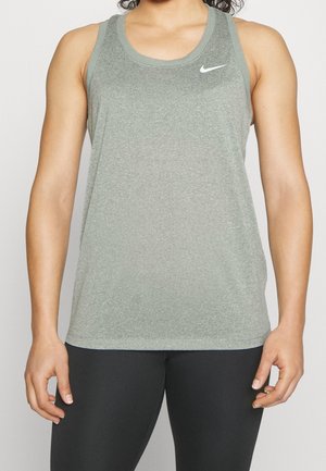 Vrouw draagt een grijze mouwloze Nike sporttop en zwarte legging tegen een effen achtergrond.