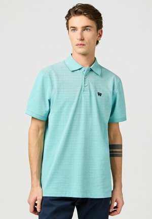 Turkusowa koszulka polo z miękkiego materiału, z klasycznym kołnierzykiem, trzema guzikami z przodu i małym logo na piersi. Krótkie rękawy.
