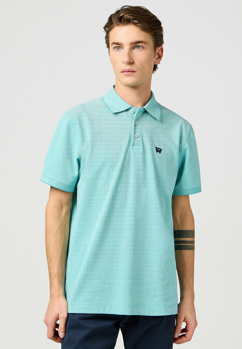 Polo shirt turchese in morbido tessuto, con colletto classico, patta con tre bottoni e un piccolo logo sul petto. Maniche corte.