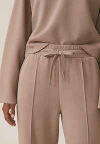 Lichtbeige, zachte stoffen trainingsbroeken met een elastische tailleband en trekkoord. Kenmerkt zich door voorplooien en een relaxed fit.