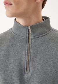 Pullover grigio a mezza zip realizzato in tessuto morbido. Presenta un colletto a coste e una zip metallica. Design semplice senza motivi o grafiche.