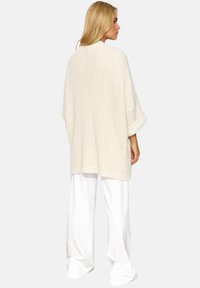 Długi, oversize'owy kremowy kardigan z textured knit pattern, o rękawach trzy czwarte i luźnym kroju, uzupełniony białymi spodniami w szerokim kroju.