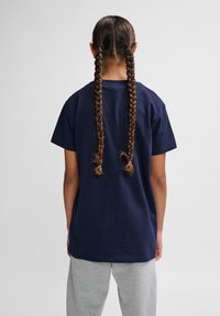 Tricou din bumbac de culoare albastru marin, cu o croială lejeră, mâneci scurte și un guler rotund, asortat cu pantaloni de trening gri. Părul prins în două codițe.
