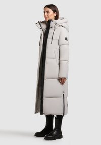 Long, puffy, light gray coat with a hood, black zipper, and two front pockets. Features a sleek silhouette and textured material.