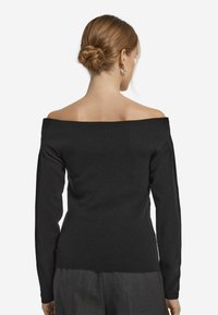 Czarny sweter typu off-the-shoulder, o żebrowanej fakturze, z długimi rękawami, dopasowany fason, podkreślający sylwetkę bez dodatkowych detali czy wzorów.