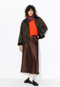 Veste en imprimé léopard marron, pull orange, jupe en satin marron et mocassins noirs. Accessoirisé avec des chaussettes blanches avec un texte rouge.