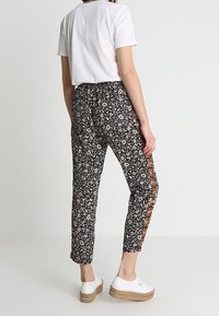 Zwarte broek met een bloemenmotief en zijkantstripes, gecombineerd met een witte blouse met korte mouwen en witte platform schoenen.