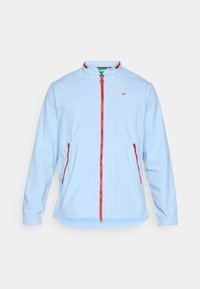 Chaqueta azul clara con cuello alzado, cremallera roja y detalles rojos a juego. Presenta mangas largas y bolsillos laterales.