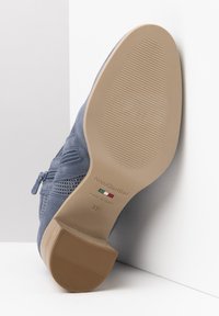 Bottine en suede bleue avec une surface texturée, fermeture éclair sur le côté et un talon moyen. La semelle est beige avec un motif strié, étiquetée "NeroGiardini."