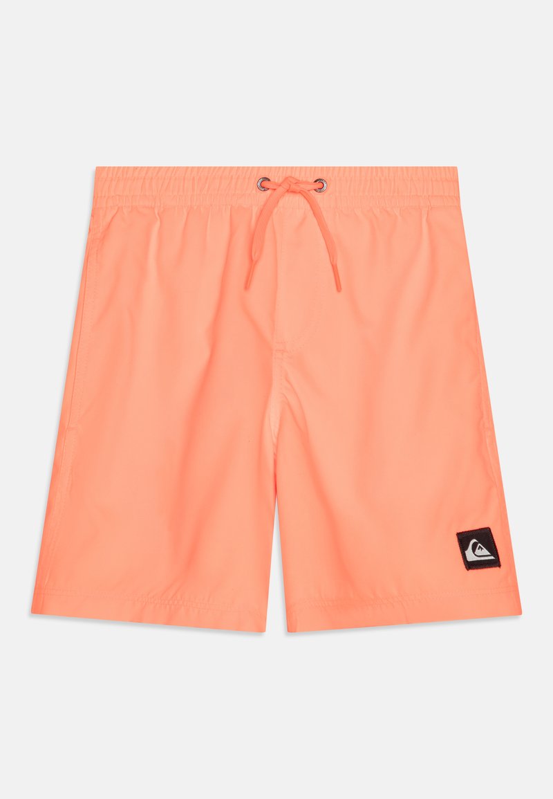 Coral swim shorts featuring an elastic waistband with drawstring, smooth texture, and a black logo patch on the lower left side.