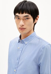 Light blue button-down shirt made of textured fabric, featuring a small embroidered detail on the chest and a classic collar design.