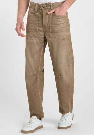 Brown denim pants with a loose fit, featuring two front pockets and a drawstring waist; paired with white sneakers for contrast.