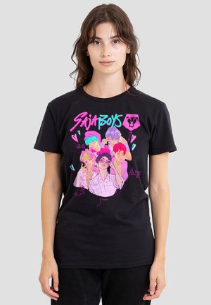 Woman wearing a black t-shirt with colorful illustrated characters and the text "Saiba Boys" in neon pink and blue on front.