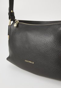 Borsa a spalla in pelle nera con superficie textured, hardware dorato e logo del marchio in rilievo. Presenta una chiusura con zip e tracolla regolabile.