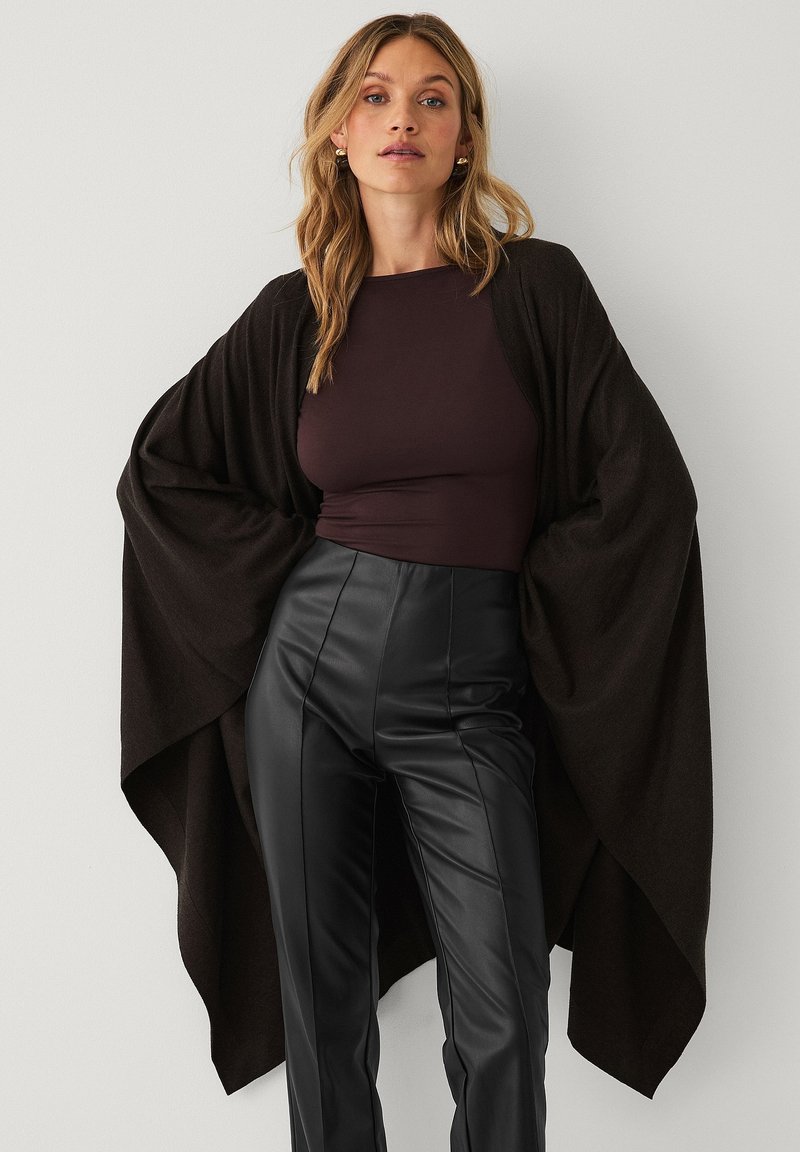 Brun kimono-stil omslag lavet af blødt stof, med brede ærmer og åben front, parret med højtaljede sorte læderbukser.