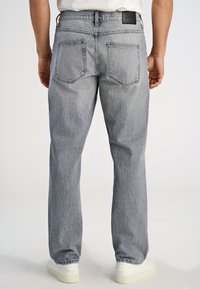 Jasnoszare jeansy z denimu o prostym kroju, z charakterystycznymi tylnymi kieszeniami i czarną skórzaną naszywką na pasku talii. Materiał o fakturze z subtelnym wypraniem.