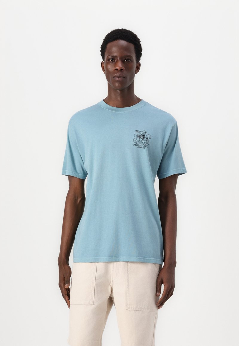 Helles blaues T-Shirt mit kurzen Ärmeln aus Baumwolle, das ein kleines schwarzes grafisches Design auf der Brust aufweist. Rundhalsausschnitt und lockere Passform.