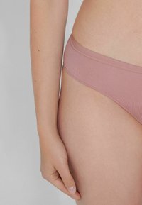 Světle růžové plavkové kalhotky vyrobené z elastického materiálu, s hladkou texturou a nízkým pasem se jednoduchým páskem.