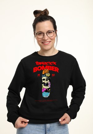 Sort sweatshirt med et farverigt grafik, der viser et skelet, blomstermønstre og tekst. Detaljer inkluderer fed rød skrift og en afslappet pasform.