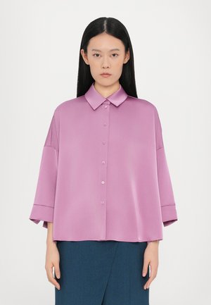 Løs-fastholdende, kortermet skjorte i pastell rosa satin med spiss krage og knappestolpe foran. Glatt tekstur med rullede mansjettdetaljer.