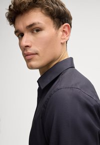 Herrenhemd mit dunklem Muster und strukturiertem Kragen, aus texturiertem Stoff und im Slim-Fit-Design, seitlich betrachtet.