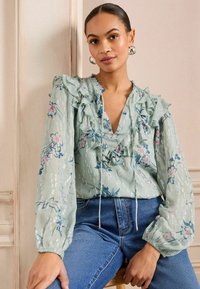 Gėlių raštas, šviesiai žalias palaidinės viršus su raukiniais rankovėmis ir V formos iškirpte. Minkšta medžiaga su struktūriniu paviršiumi. Derinama su aukšto juosmens džinsais.