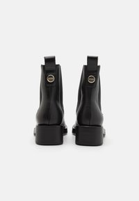 Mustad mustad rinna saapad nelinurga varbaga ja plokiahnaga, millel on kuldse tooni logo aktsent tagumisel tõmbeantral. Sile tekstuur.