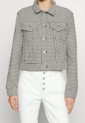 Chaqueta recortada en blanco y negro con estampado de espiga, con botones al frente, bolsillos en el pecho y cuello. Llevada con pantalones de mezclilla blanca de cintura alta.