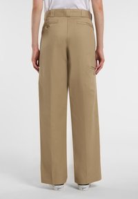 Kaki vida byxor med en slät yta, med två bakfickor och logodetalj, stiliserade med en vit topp och sneakers.