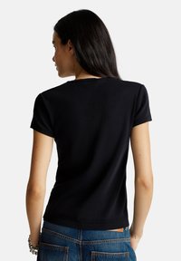 Top nero a maniche corte con texture a coste, scollatura rotonda e design aderente che si stringe in vita. Finitura semplice e pulita.