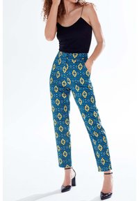 Blue patterned pants with diamond motifs in yellow and black, featuring a high waist and side pockets, styled with a black top and heels.