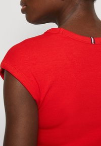 Punainen ribattu t-paita, jossa on lyhyet käärityt hihat ja erottuva raidallinen yksityiskohta niskassa. Sujuva pinta.